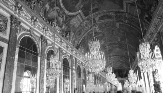 Schwarz-Weiß-Foto des Spiegelsaals von Versailles. Links Spiegel, oben mehrere Kronleuchter und ein Deckengemälde. Die Fenster rechts sind nur noch andeutungsweise zu sehen.